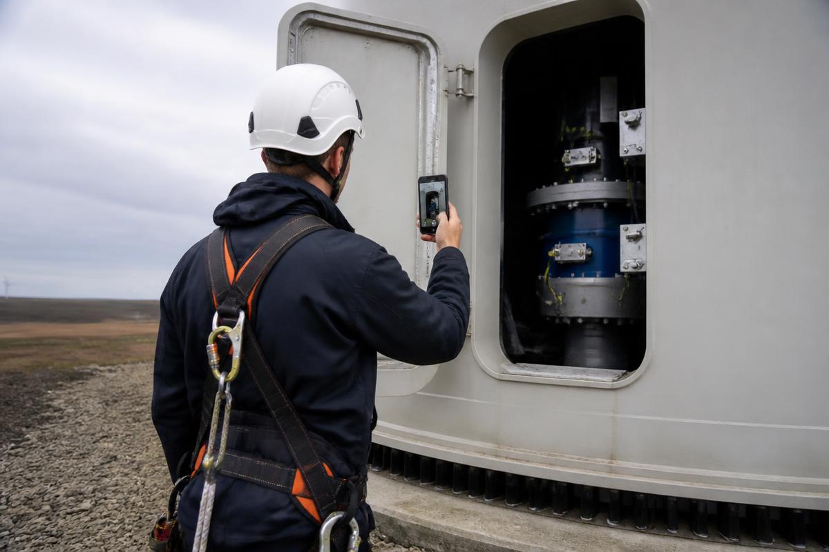 Wind turbine technician filming components inside the turbine tower with a smartphone
